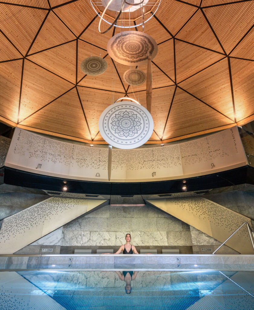 Wellnessbereich im Mountain Resort Feuerberg in Kärnten mit Indoor-Pool, moderner Architektur und kunstvoller Holzkuppel.