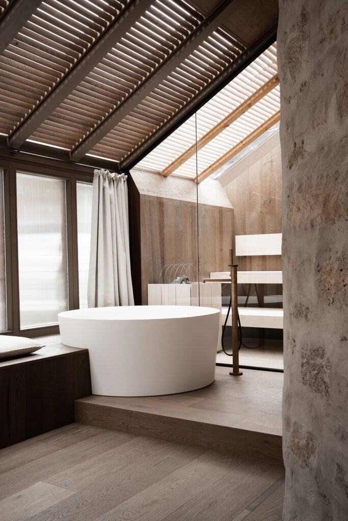 Luxuriöses Badezimmer im Hotel stiegnhaus mit freistehender Badewanne, natürlichem Holz-Design und Tageslicht durch Dachfenster.